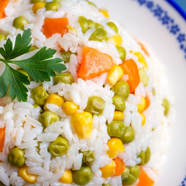 Close-up of Istanbul Kitchen's Mediterranean rice pilaf with peas, carrots, and corn, garnished with parsley.