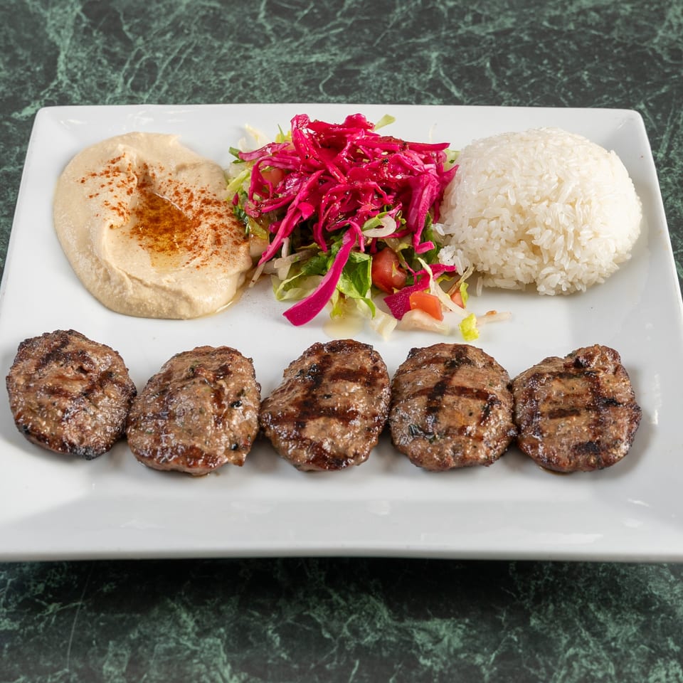 Grilled meat patties with hummus, red cabbage salad, and white rice on a rectangular plate.