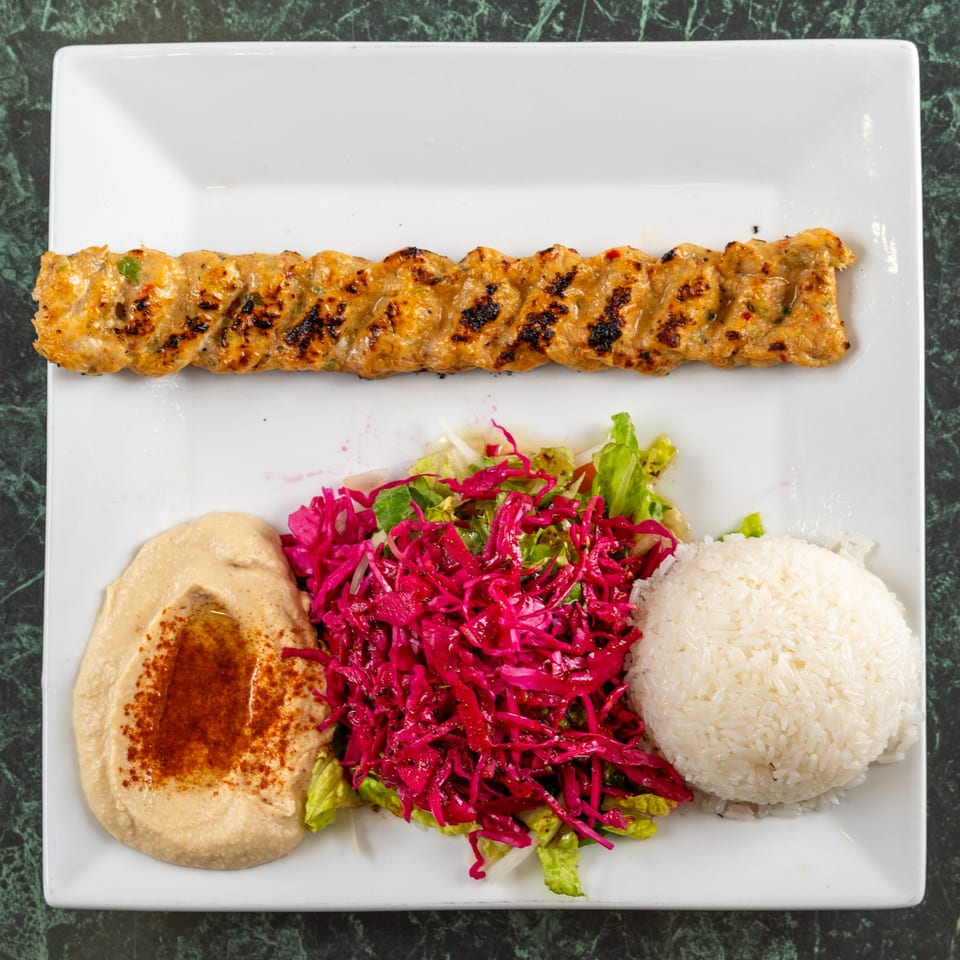 Grilled Adana kebab, hummus, rice, and red cabbage salad on a white plate from Istanbul Kitchen.