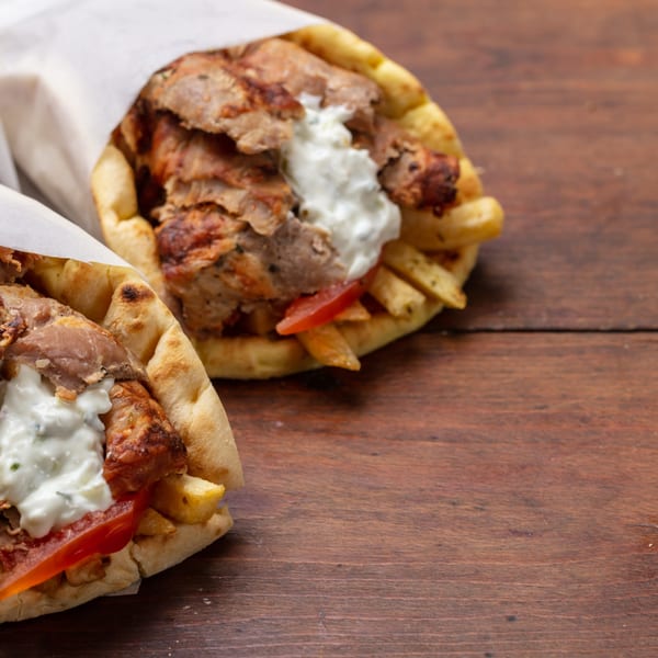 Two delicious Mediterranean gyros with meat, fries, tomatoes, and tzatziki sauce on a wooden table.